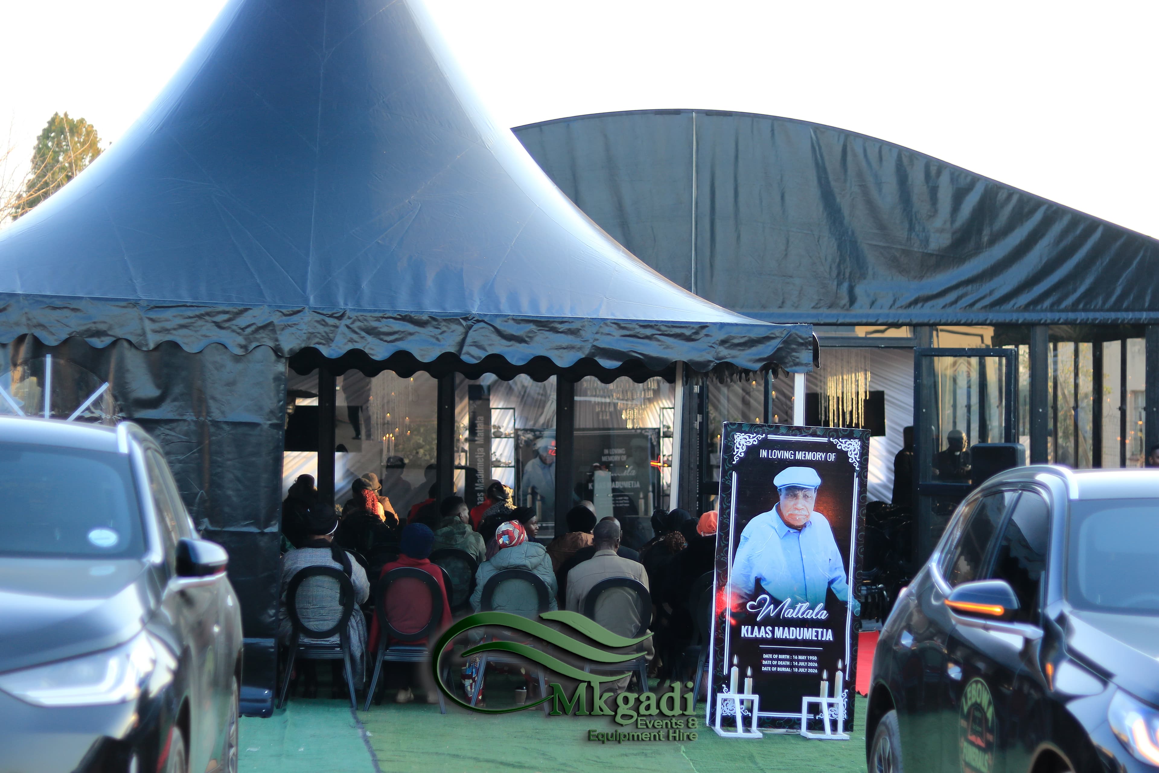Outdoor funeral setup with black pagoda tents, rows of chairs and memorial banners celebrating a life well lived