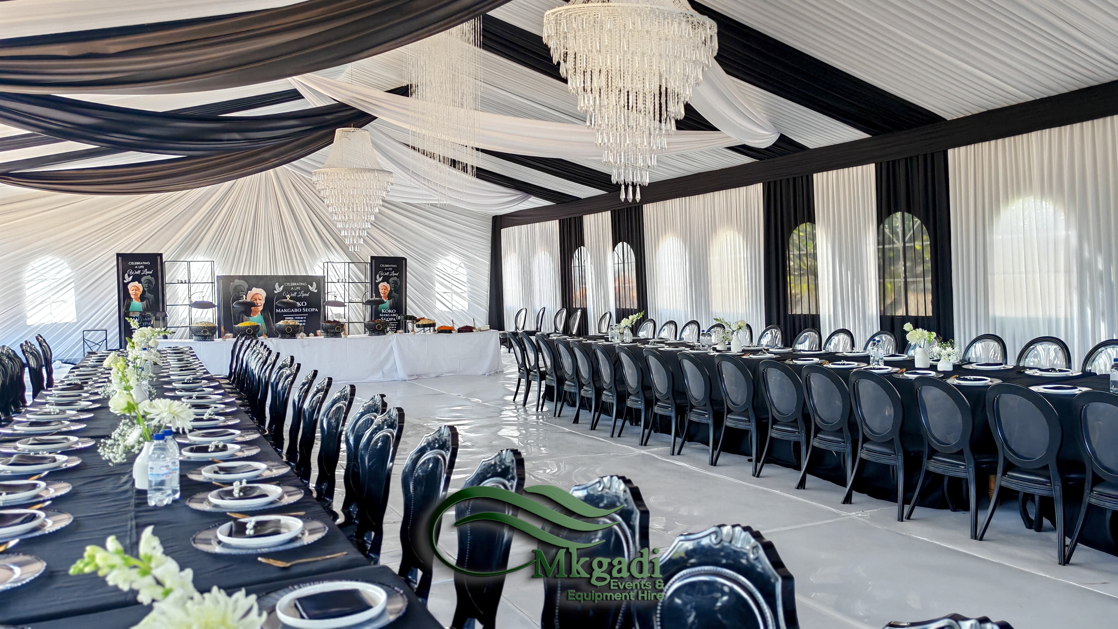 Styled event corner with lush floral arrangements, draped fabric backdrop and decorative lighting for a wedding or gala