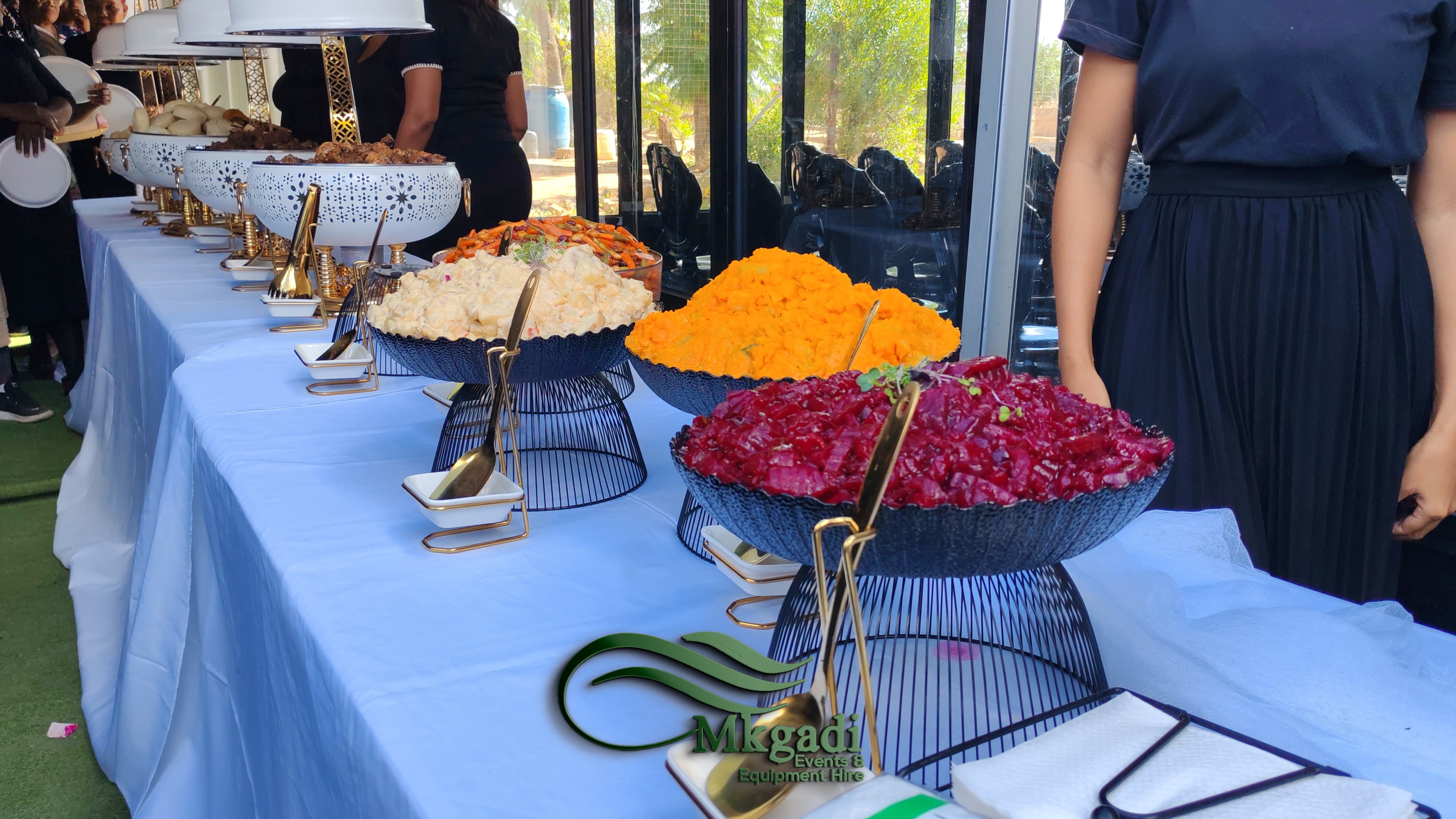 Professional catering buffet spread with colourful salads and gold cutlery on a long white linen table at a Mkgadi Events function