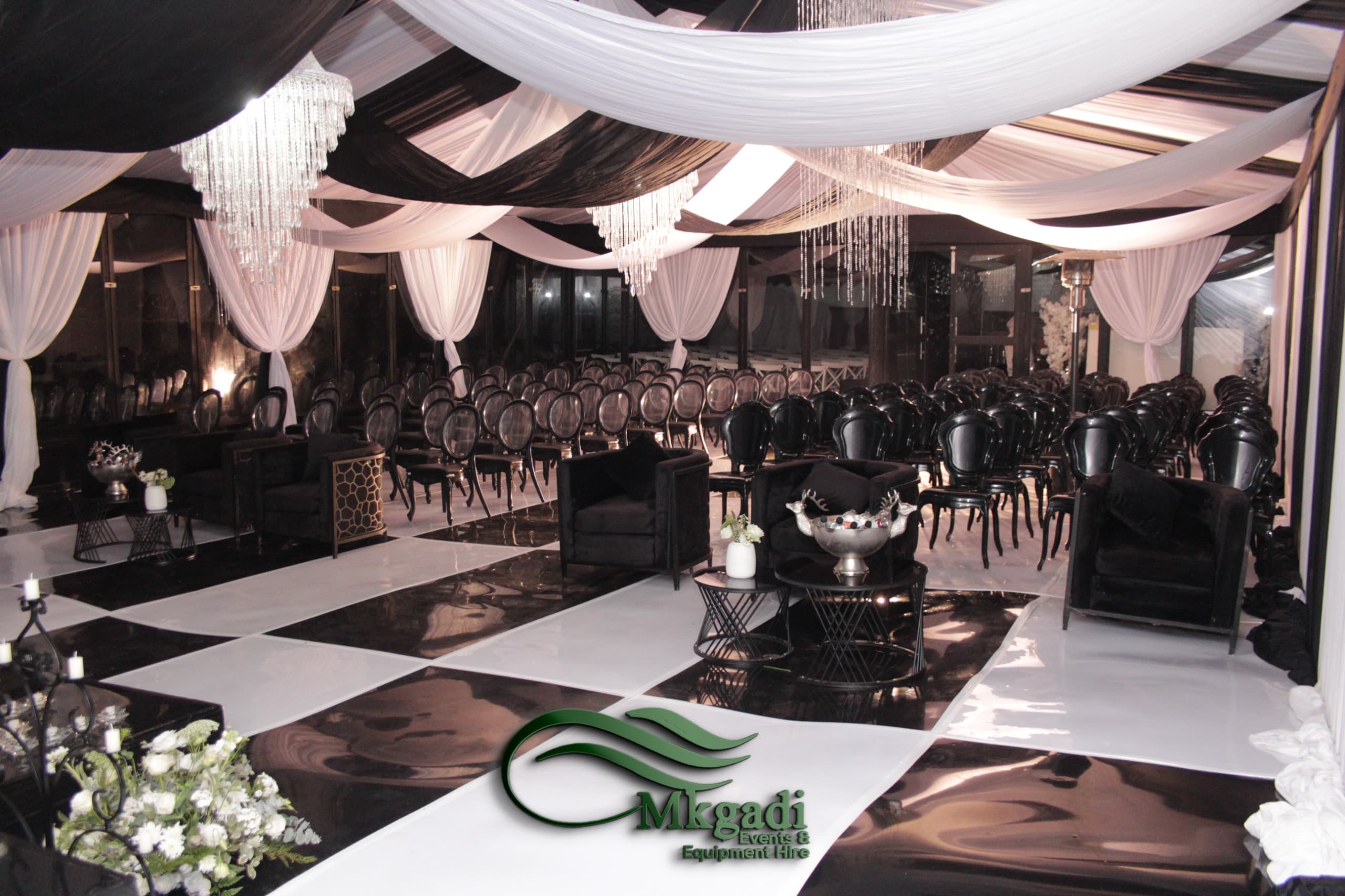 Stunning black and white wedding venue with crystal chandeliers, dramatic draping, black Chiavari chairs and a chequered dance floor